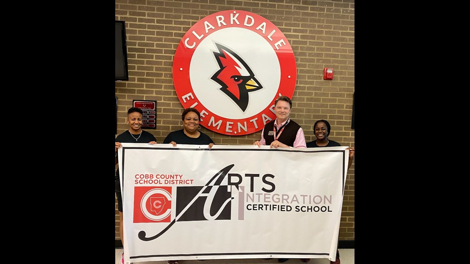 4 people holding the Arts Integration banner in front of our school logo 